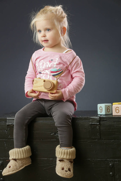 Studio portrait of adorable two years old toddler girl in pink shirt with wooden camera toy - Photo, Image