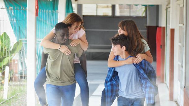 nastolatek grupa z wielu etnicznych przyjaciół w szkole mając zabawy piggybacking na zewnątrz w korytarzu. - Zdjęcie, obraz