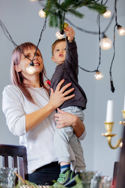 Woman with son prepares fairy lights for Christmas dinner - Фото, зображення