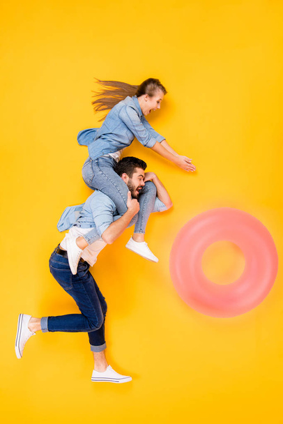 Vertical top view above high angle flat lay flatlay lie full length body size view concept of cheerful cheery spouses flying having fun isolated on bright vivid shine vibrant yellow color background - Photo, image