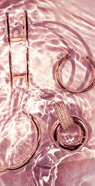 Rose gold bracelets, earrings, rings, jewelery on pink water bac - Photo, Image
