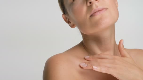 Close-up beauty portrait of young woman with smooth healthy skin, she gently touches her shoulders with her fingers on white background and smiles - Filmagem, Vídeo