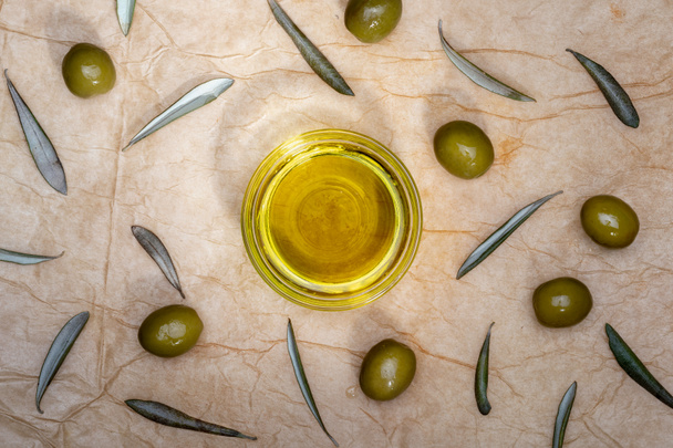 Aceite de oliva virgen extra en un recipiente de vidrio. Incluye hojas y ramas de olivo. Fondo rústico. Vista superior. - Foto, imagen