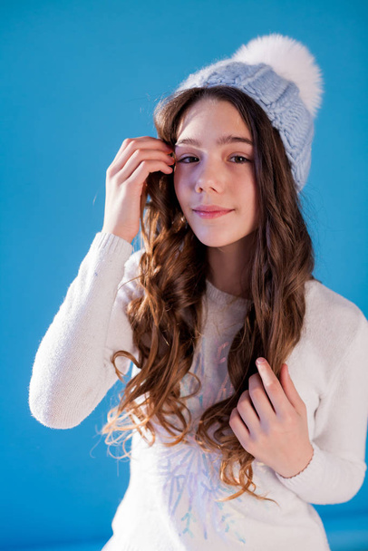 Beautiful fashionable girl in winter snow cap blue background - Photo, Image