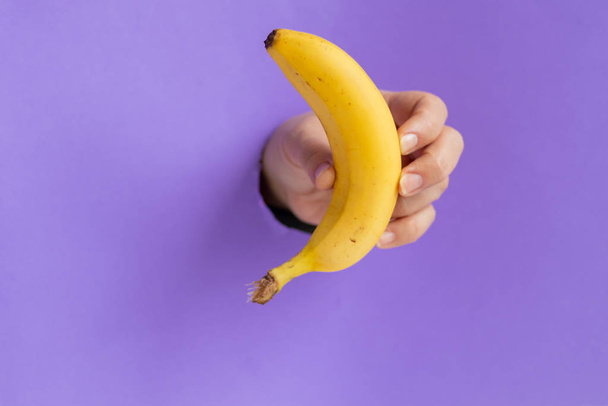 女性の手にはバナナがある。紙のシートに穴に挿入されます。健康的な食事コピースペース.  - 写真・画像