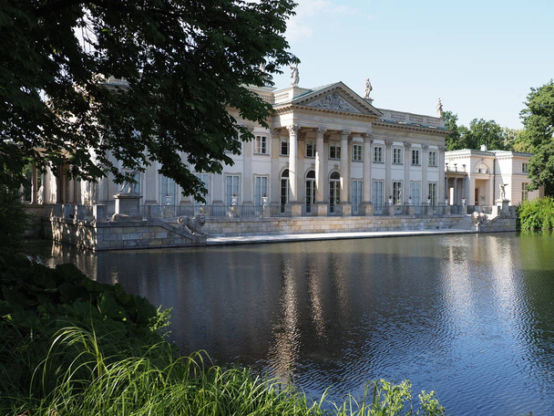 Palace on isle reflected in water behind bough at lake in baths park in Warsaw european capital city of Poland, clear blue sky in 2019 warm sunny spring morning day on July. - 写真・画像