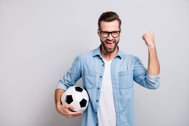 Photo of attractive handsome guy holding leather white black soccer ball yelling loud supporting team football match wear specs casual denim outfit isolated grey color background - Photo, Image