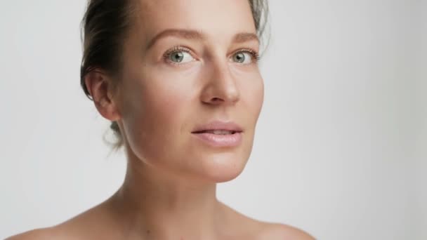 Close-up beauty portrait of young woman with smooth healthy skin, she gently touches her face with her fingers on white background and smiles - Filmagem, Vídeo