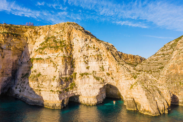 Vista aérea de cuevas, acantilados. Cielo azul claro, rocas, bote. Malta país
 - Foto, imagen