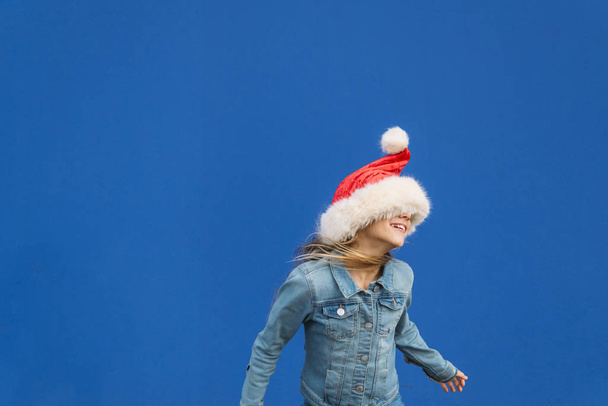 Niña rubia bailando con un sombrero de Santa. Feliz Navidad.
! - Foto, Imagen
