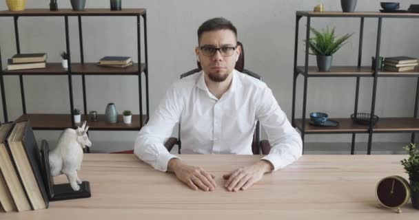 Young man office worker in glasses sitting at table and looking at camera. - Filmmaterial, Video