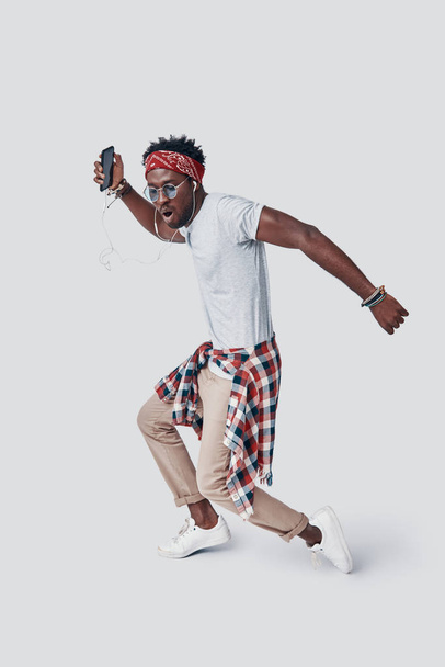 Full length of handsome young African man dancing and making a face while standing against grey background - Foto, afbeelding
