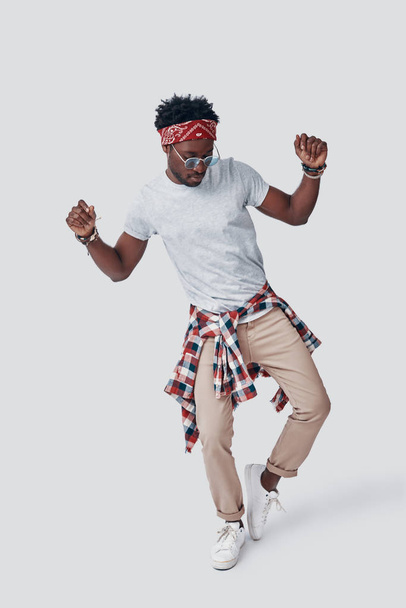 Pełna długość zabawy młody Afrykanin tańczy stojąc na szarym tle - Zdjęcie, obraz