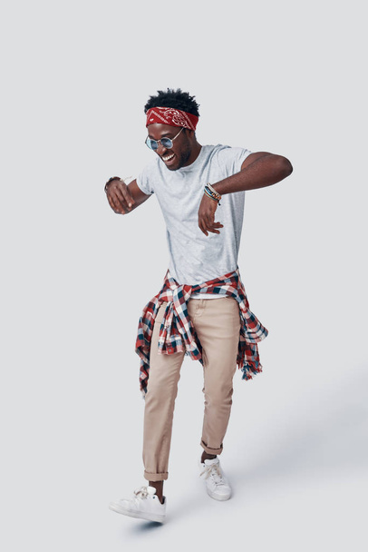 Full length of playful young African man dancing and smiling while standing against grey background - Zdjęcie, obraz