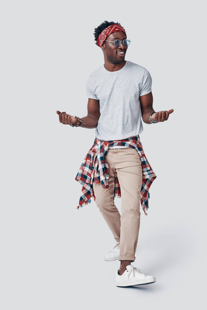 Full length of playful young African man dancing and smiling while standing against grey background - Photo, Image
