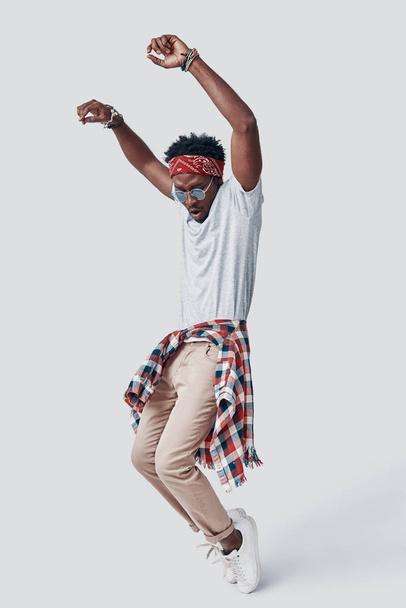 Full length of playful young African man dancing while standing against grey background - Foto, afbeelding