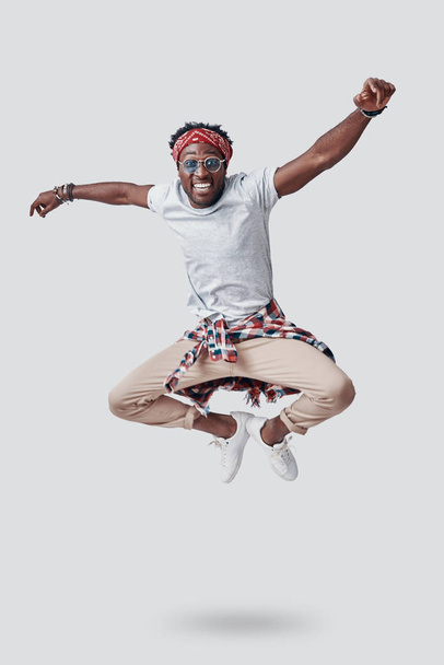 Full length of playful young African looking at camera and smiling while hovering against grey background - Foto, Imagem