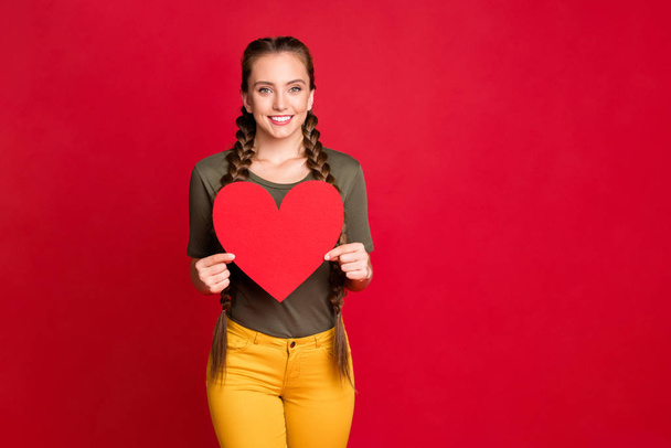 Photo of pretty lady holding big paper heart showing amazing prom invitation postcard wear casual yellow pants green t-shirt isolated red color background - Zdjęcie, obraz