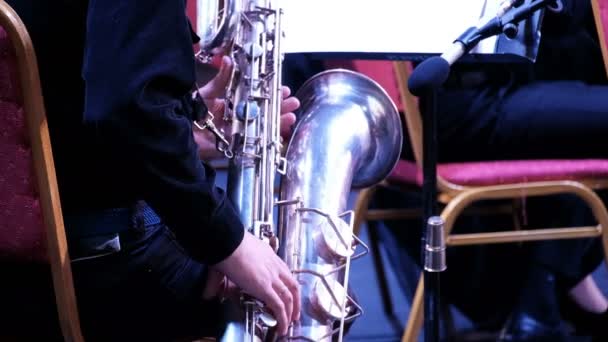 Een mans hand in een zwart pak op een grote saxofoon in een jazzband. Muzikant van een fanfare. Feestelijk concert van het symfonieorkest. Muzikant van een fanfare. Concert. Een close-up. Achteraanzicht. - Video