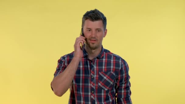 Pleasant-looking young man speaking with somebody by smartphone on yellow background. - Materiał filmowy, wideo