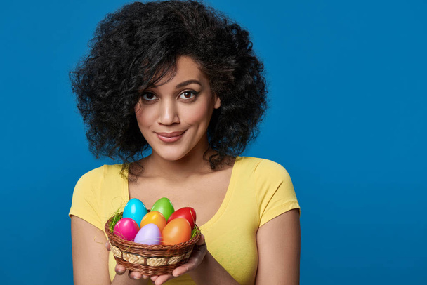 Smiling woman holding a basket with colorful Easter eggs - Fotoğraf, Görsel