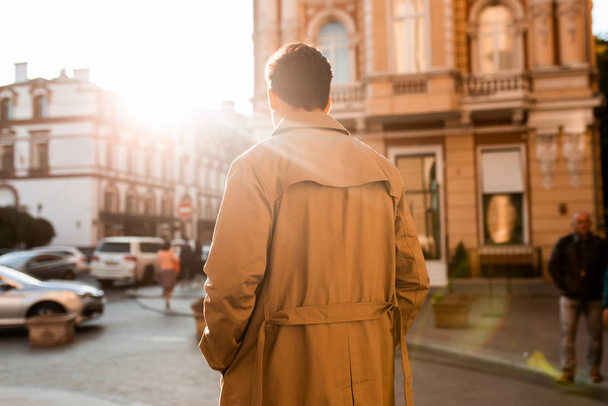 Vista trasera del joven hombre confiado en gabardina caminando por la calle de la ciudad solo
 - Foto, imagen