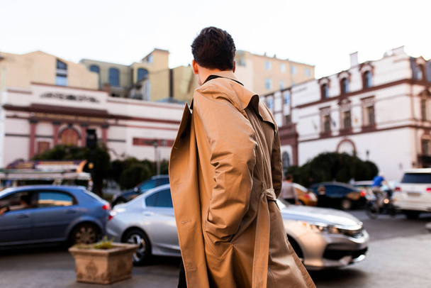Trençkotlu genç bir adamın şehir caddesinde yürüyüşünün arkası.  - Fotoğraf, Görsel