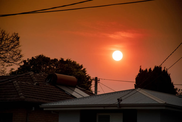 Feu de brousse australien : la fumée des feux de brousse couvre le ciel et le coucher de soleil jaune et rouge au-dessus des toits a l'air effrayant. Banlieue dans un brouillard de fumée. Catastrophic fire danger, NSW, Australie
 - Photo, image