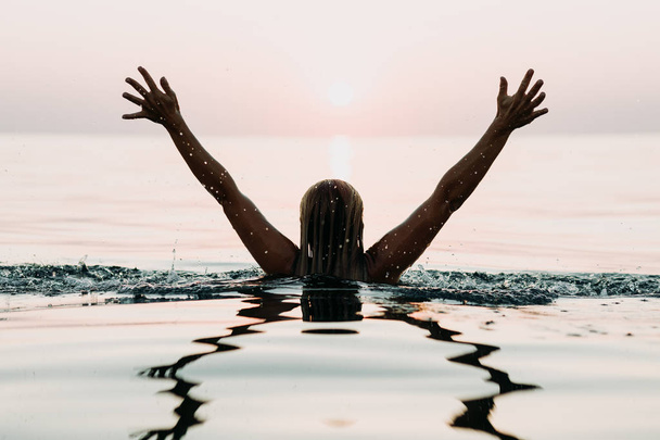 Woman in the sea looking in sunset with arms above the water - Foto, immagini