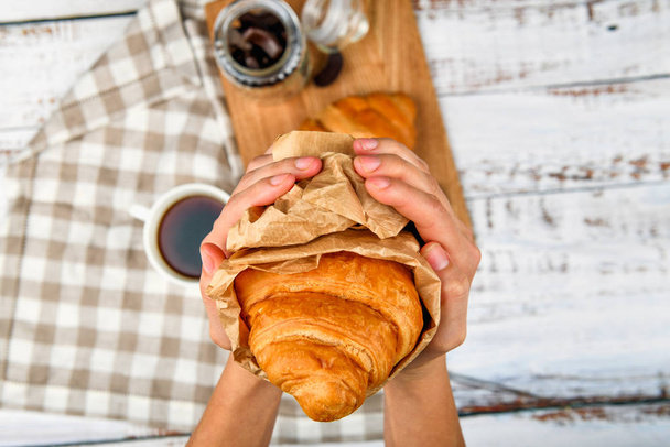 croissant nelle mani. Primo piano di croissant gustoso nelle mani. su uno sfondo piatto. carta velina avvolta - Foto, immagini