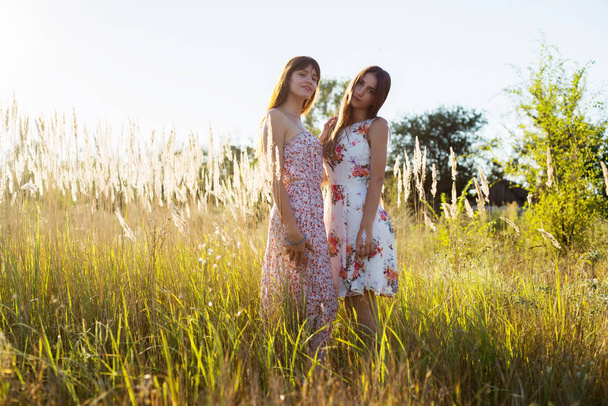 Two girls in floral dresses, sisters, girlfriends, friends posing at summer nature background together - Fotó, kép