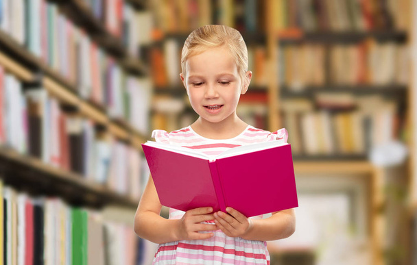 smiling little girl reading book at library - Foto, Imagem