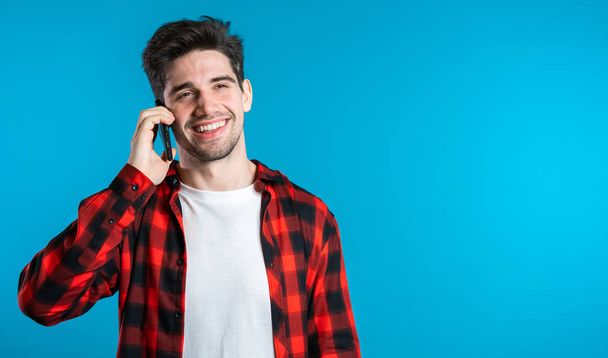 Young man in bright colorful wear talking on mobile cell phone on blue background. Trendy guy have conversation. Smartphone, technology concept. - Zdjęcie, obraz