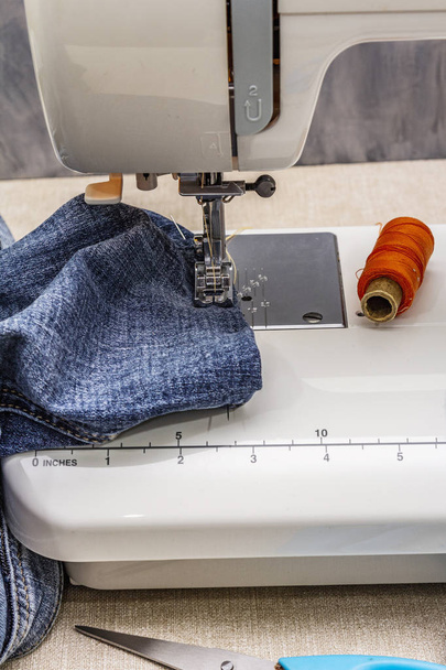 Pie de máquina de coser en el denim. Tijeras, carretes de hilo. Se levanta sobre una mesa, fondo de madera
 - Foto, Imagen