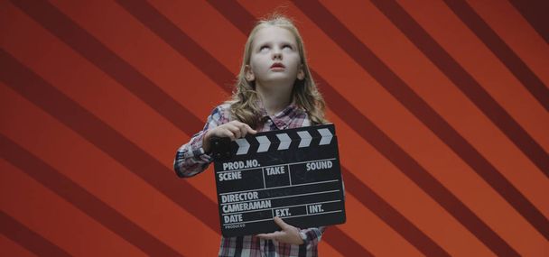 Girl clapping clapboard and raising eyebrows - Photo, Image