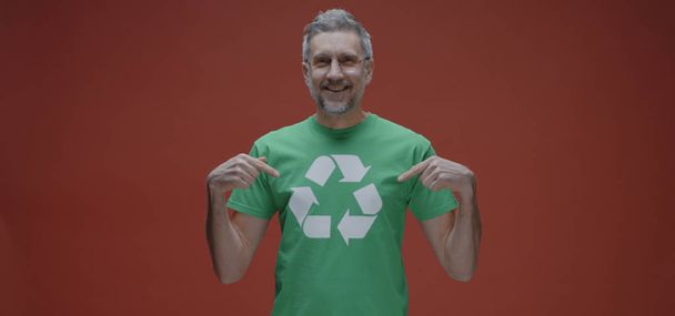 Мужчина указывает на символ вторичной переработки на футболке
 - Фото, изображение