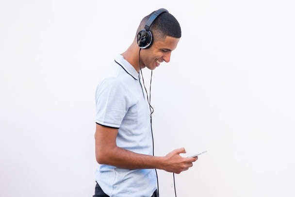 Side muotokuva onnellinen Pohjois-Afrikkalainen mies kuuntelee musiikkia kuulokkeet ja matkapuhelin valkoisella taustalla
 - Valokuva, kuva