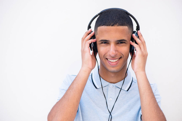 Close up portrait of smiling young man listening to music with headphones by white background - Foto, Imagem