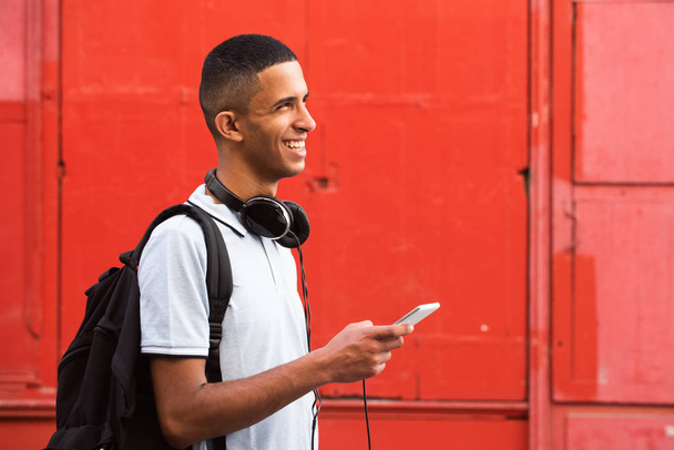 Close up ritratto laterale di sorridente arabo studente maschio con telefono cellulare e borsa da sfondo rosso
 - Foto, immagini
