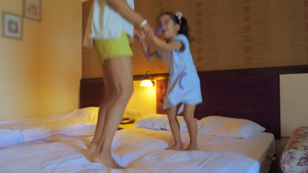 Mom and daughter jump on the bed in the hotel room. - Video