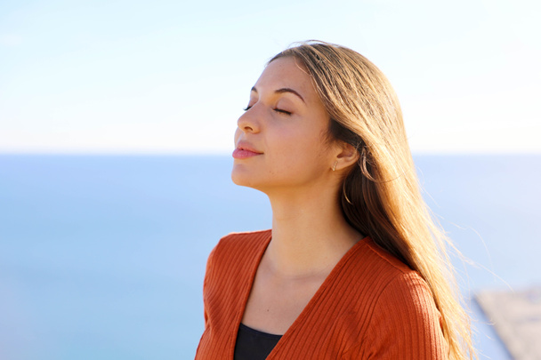 Close up of beautiful relaxed girl breathing fresh air with blue sea on the background. - Photo, Image