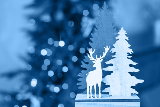 Класичний синій колір 2020 року. Різдвяні сувеніри дерев'яні ялинки та олені на тлі різдвяних новорічних вогнів. Різдвяна листівка. Копіювальний простір - Фото, зображення