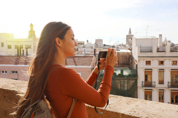 Vista lateral de la chica viajera tomando fotos desde la terraza de Valencia, España
. - Foto, Imagen