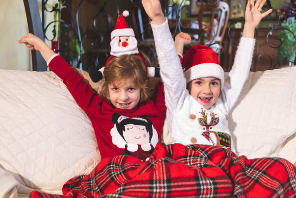 Κορίτσια που κάθονται στον καναπέ μαζί, καλυμμένα με κουβέρτα. Χριστούγεννα - Φωτογραφία, εικόνα