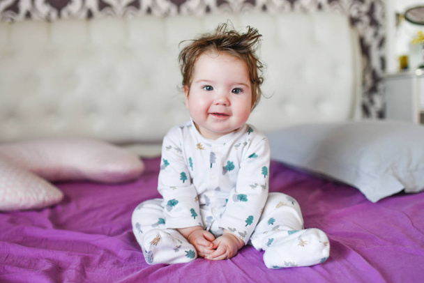 the baby is sitting on the bed. Cute girl on the bed in the bedroom - Foto, afbeelding