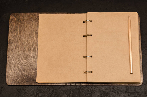Ekologický otevřený notebook v dřevěném krytu s prázdnými listy s prostorem pro váš text a tužkou na černém pozadí. Na seznam. Čas zhodnotit nebo stanovit nový koncept cílů. Mockup. Horní pohled - Fotografie, Obrázek