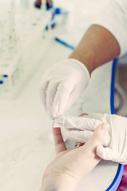 Κλείσιμο δειγματοληψίας αίματος από το δάχτυλο, τον τεχνικό εργαστηρίου και τα χέρια του ασθενούς. - Φωτογραφία, εικόνα