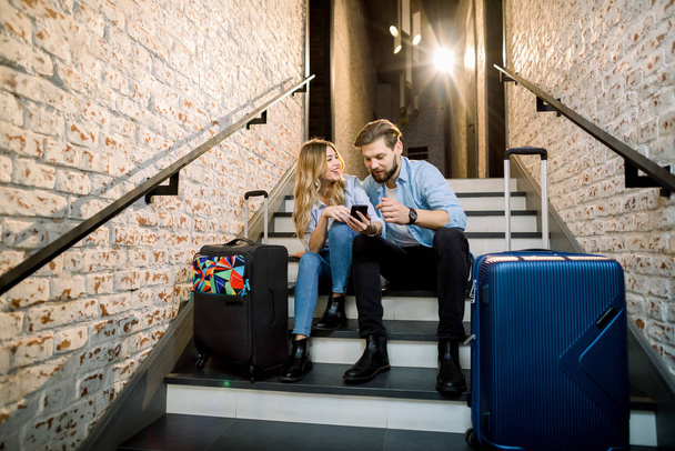 Young couple business people travelers, with suitcases, sitting at the stairs and using mobile phone - Фото, зображення