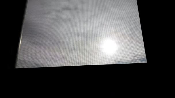 Blick aus einem dunklen Hausfenster in blauem Himmel mit großer Sonne und vielen Wolken - Filmmaterial, Video
