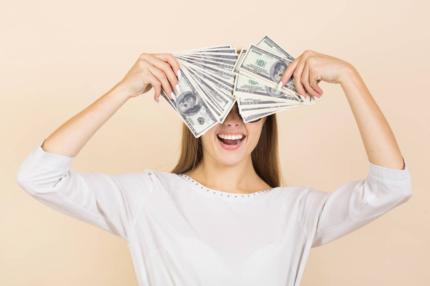 beautiful young woman in glasses on a beige background with dollars in hands - Fotó, kép